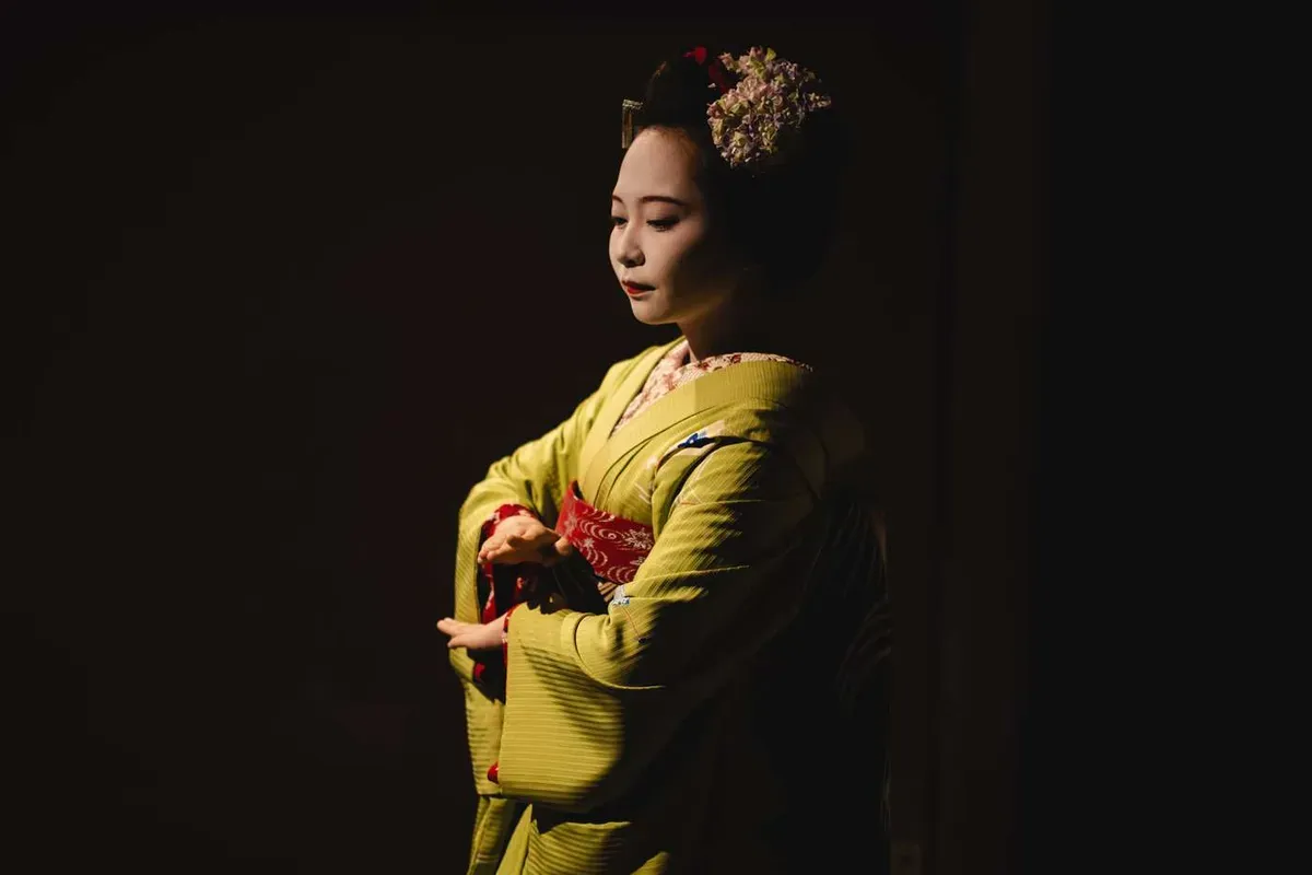 Apprentice maiko in a green kimono with floral kanzashi performing a dance during a private maiko experience in Kyoto